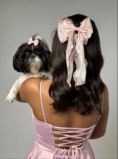 Aniversariante de 15 anos de costas com laço rosa e cachorro no ombro