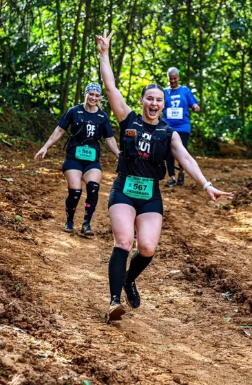 Corredora comemorando de braços abertos em trilha de trail run