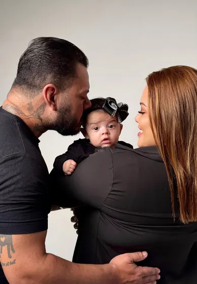 Pai beijando a testa da bebê no colo da mãe