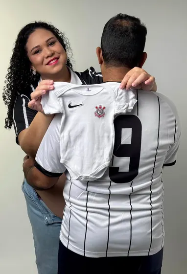 Casal em chá revelação com body de bebê do time